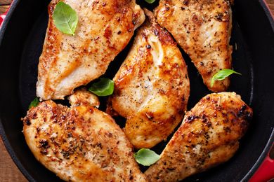 Cooked chicken breasts in a pan with a few fresh leaves as garnish