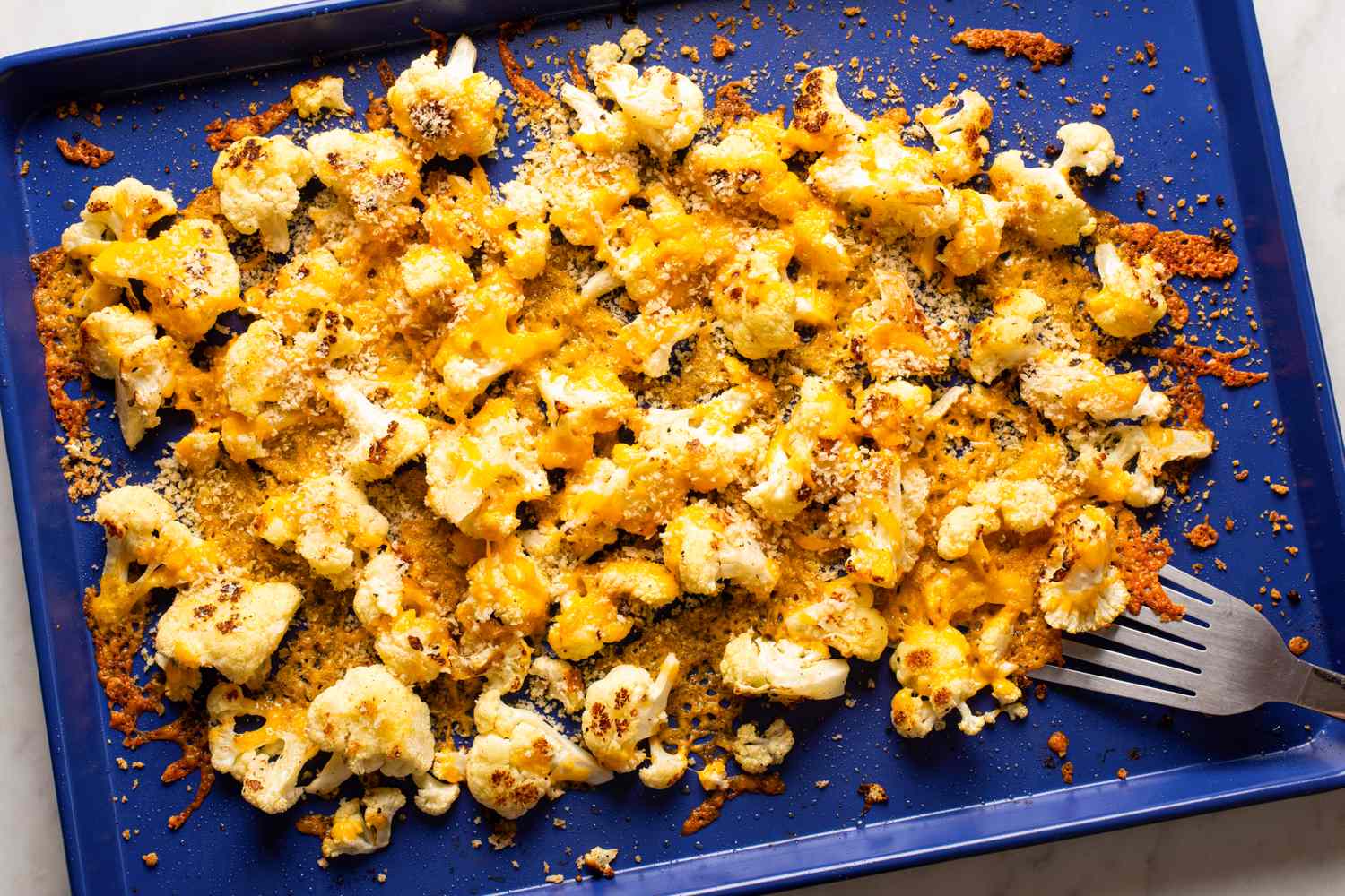 Roasted cauliflower topped with breadcrumbs and melted cheese on a baking tray accompanied by a fork