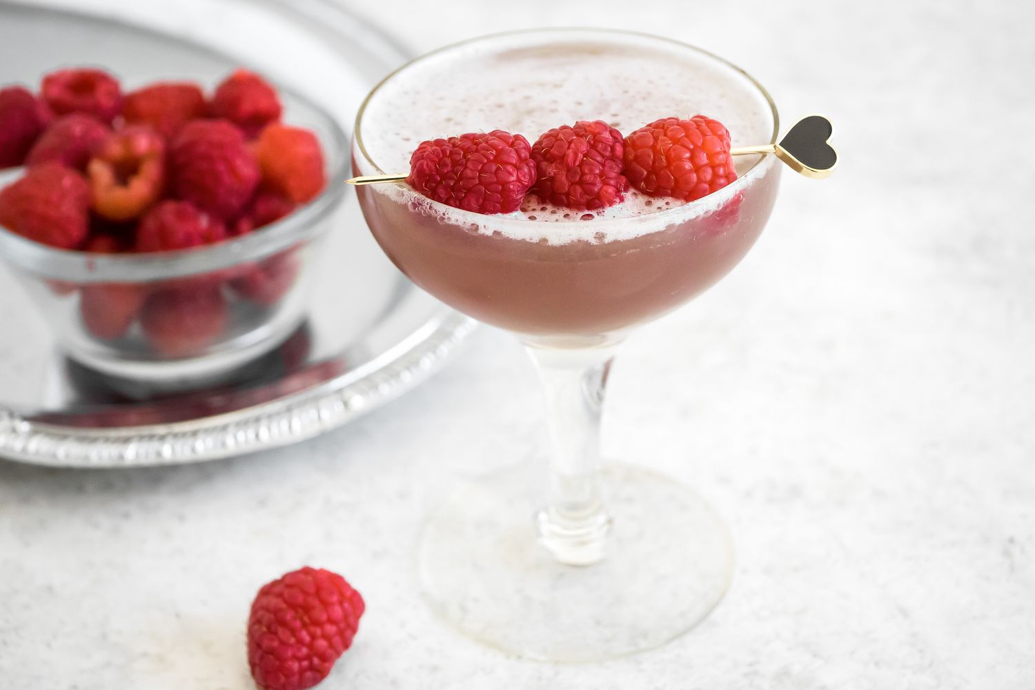 French Martini in a Glass Garnished with Raspberries in Front of a Bowl of Raspberries