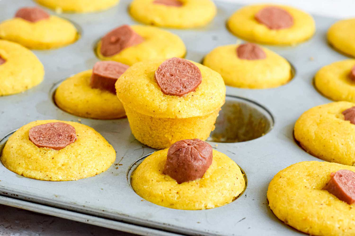 Corn Dog Muffins in a Muffin Tin With One Removed From the Muffin Hole and Placed on the Tin's Rim