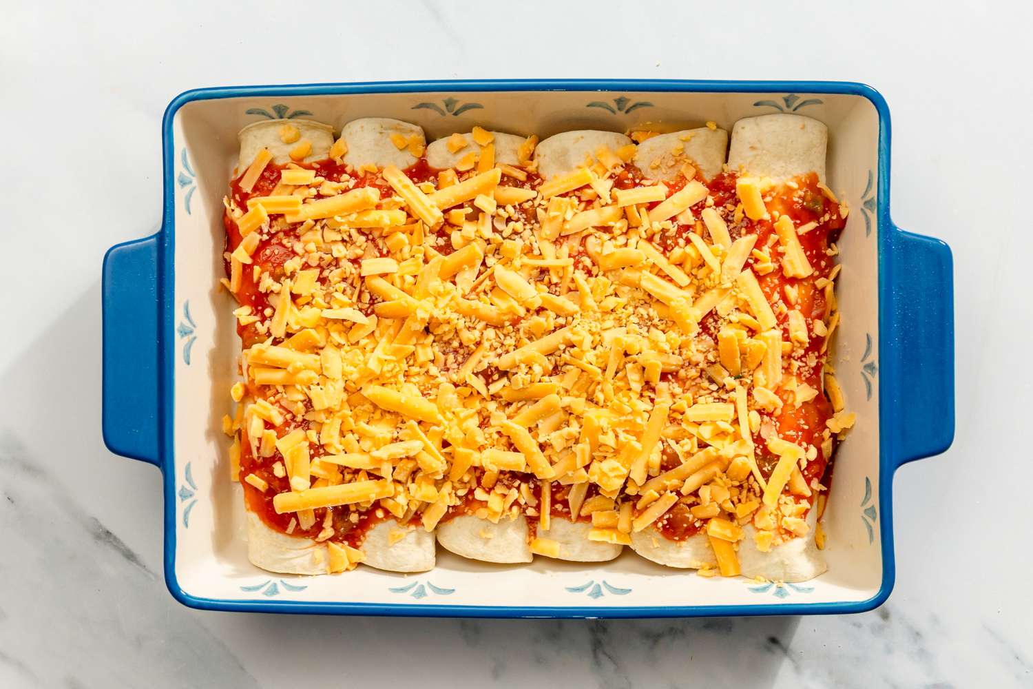 Baking dish with rolled tortillas topped with tomato sauce and shredded cheese for Chicken and Spinach Tortilla Bake recipe
