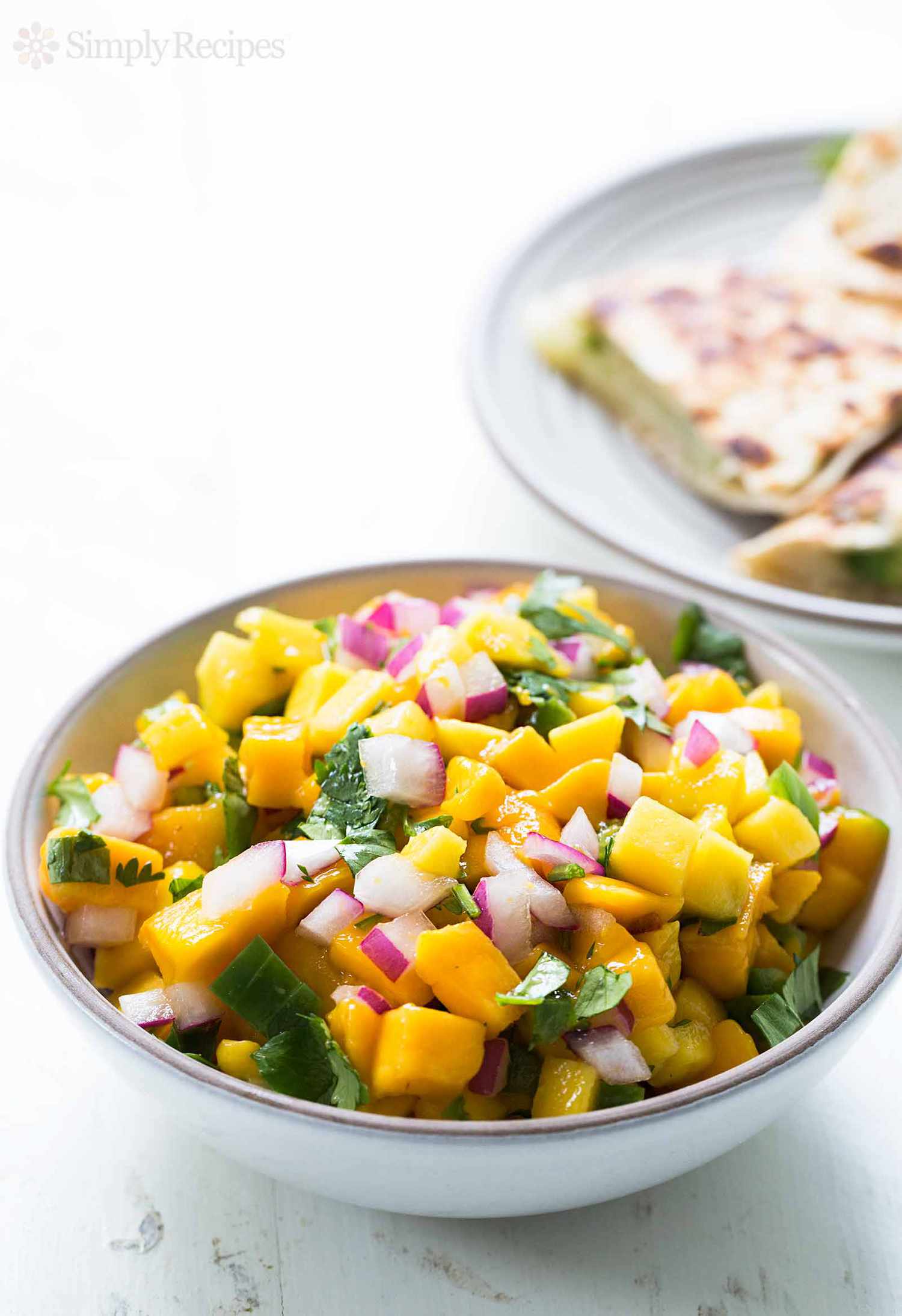 Mango Salsa in a white bowl with quesadillas in background