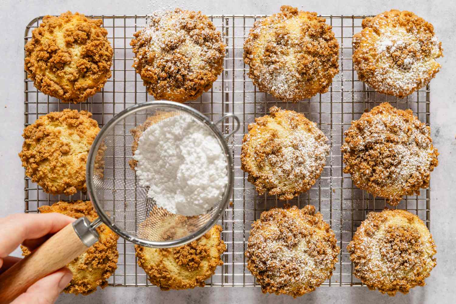 Coffee cake muffins on a cooling rack with powdered sugar being dusted on them