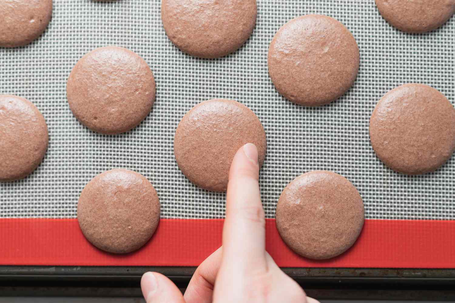Touching unbaked chocolate macaron shell.