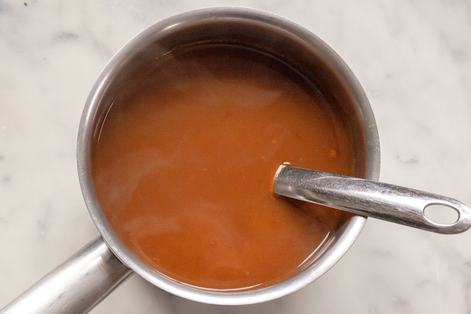 A saucepan containing brown gravy with a ladle handle resting inside it