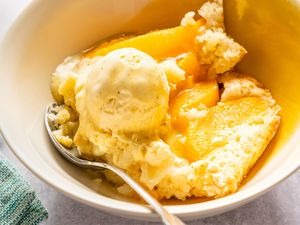 Bowl containing peach cobbler with a scoop of vanilla ice cream and a spoon