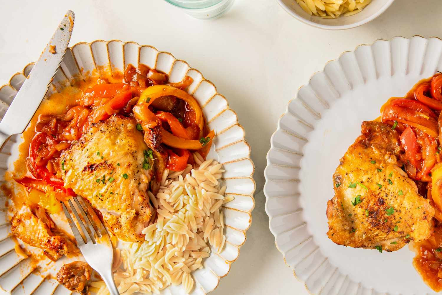 Two plates of peperonata chicken with roasted bell peppers and a side of orzo pasta