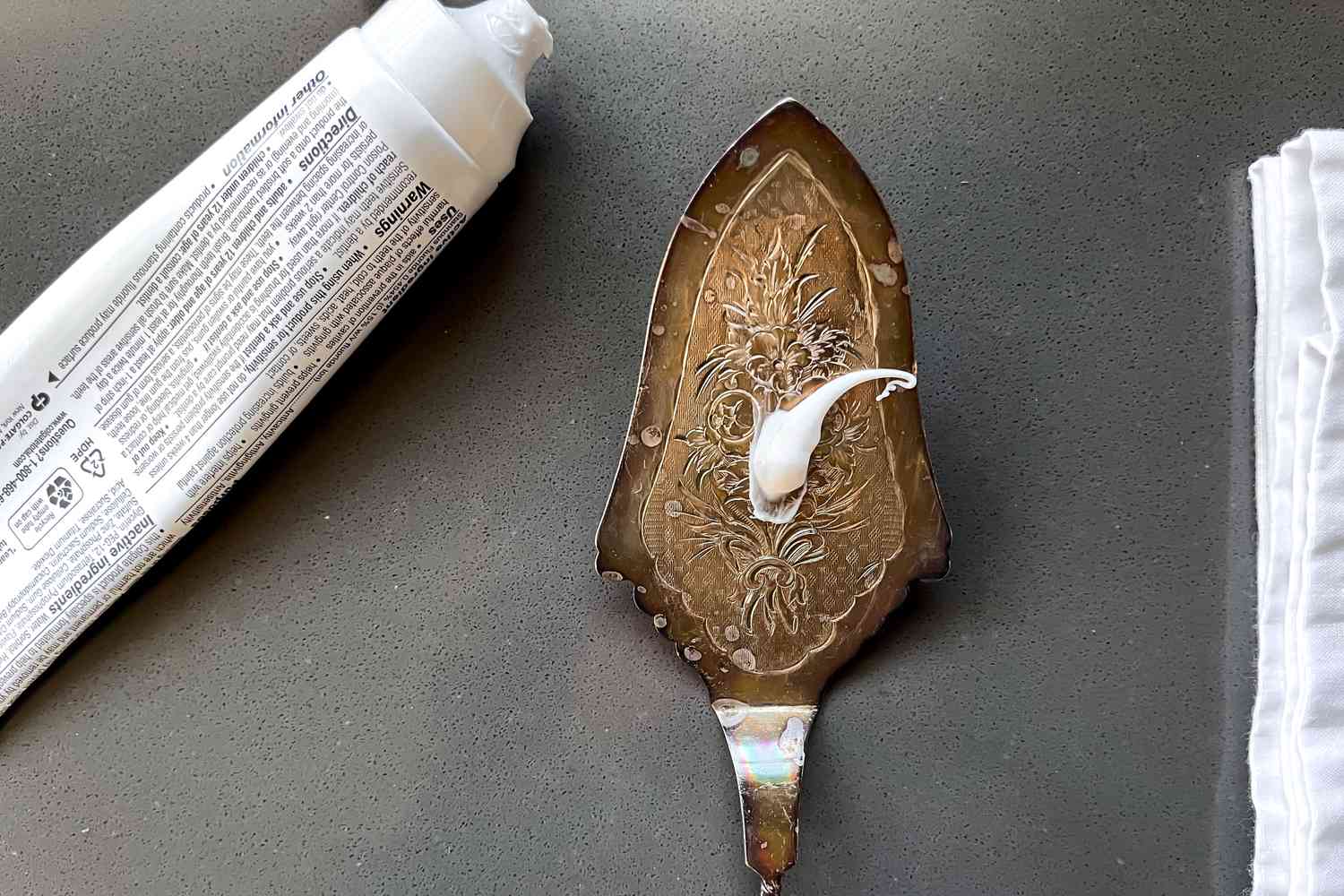 Tarnished Silver Pie Server With a Dollop of Toothpaste, and Next to It, a Table Napkin and a Tube of Toothpaste for How to Clean Silver