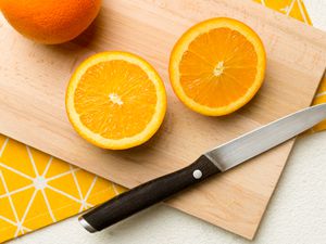 Overhead view of a sliced up orange and a knife on a wooden cutting board