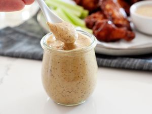 Spooning honey mustard sauce out of a glass jar.