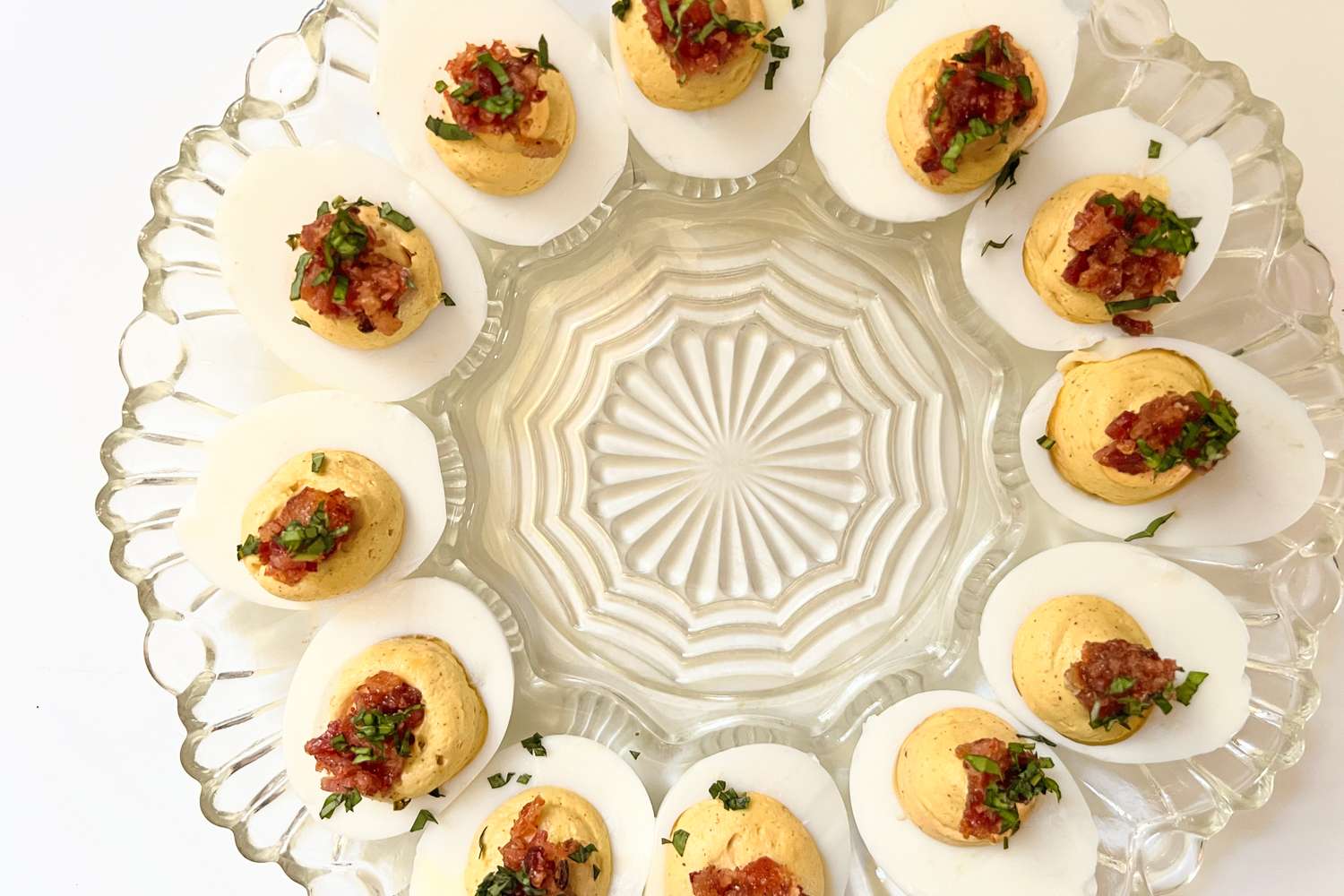 A platter of deviled eggs topped with garnishes arranged in a circular pattern on a glass serving dish