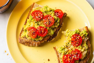 Avocado toast topped with sliced cherry tomatoes on a yellow plate