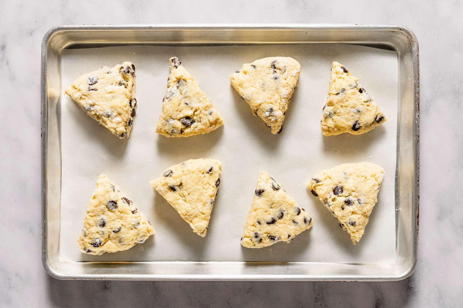 A tray of unbaked chocolate chip scones arranged on parchment paper