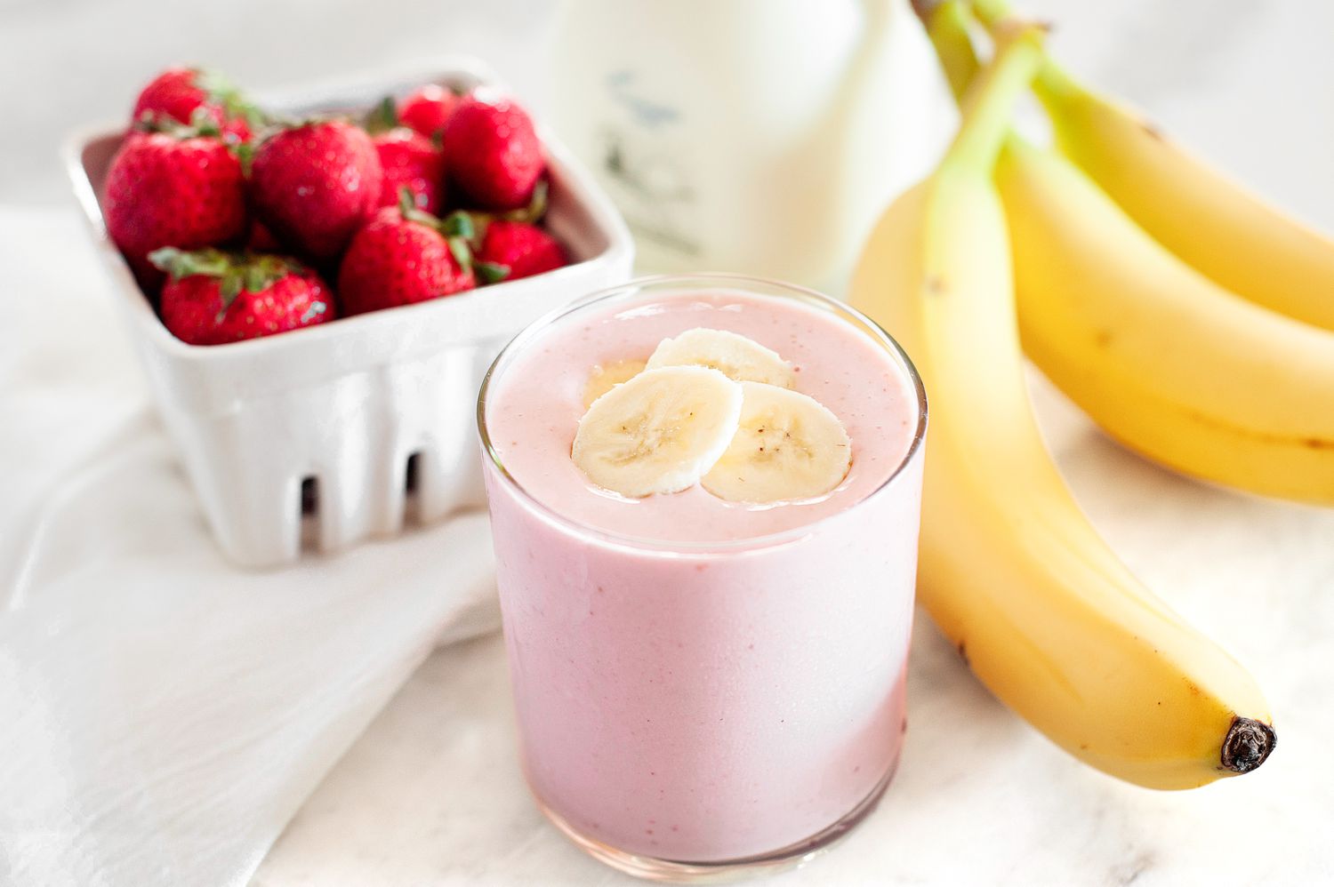 Strawberry banana smoothie in a glass with fruit in the background