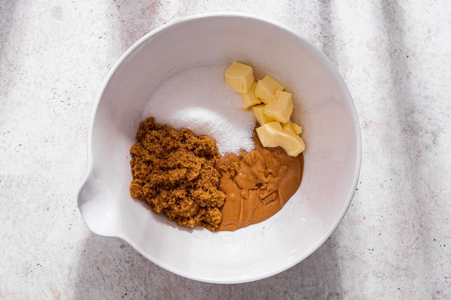 Butter, brown and white sugar, and peanut butter in a bowl for monster cookie recipe