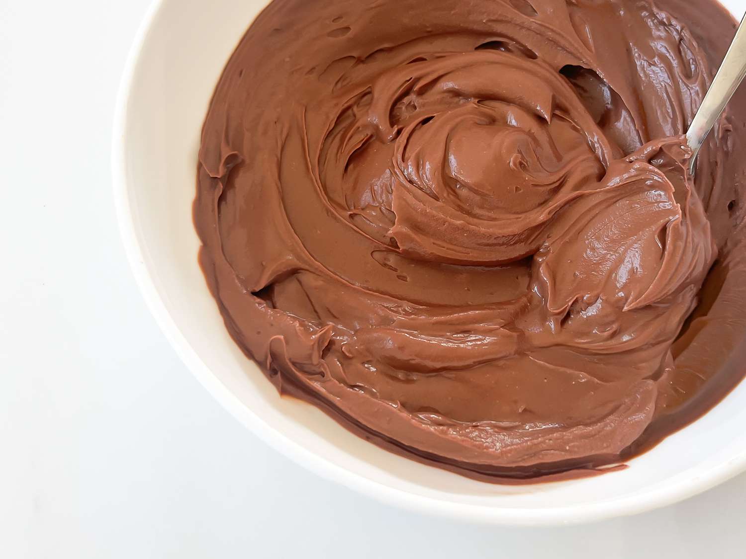 A bowl of chocolate frosting with a spoon