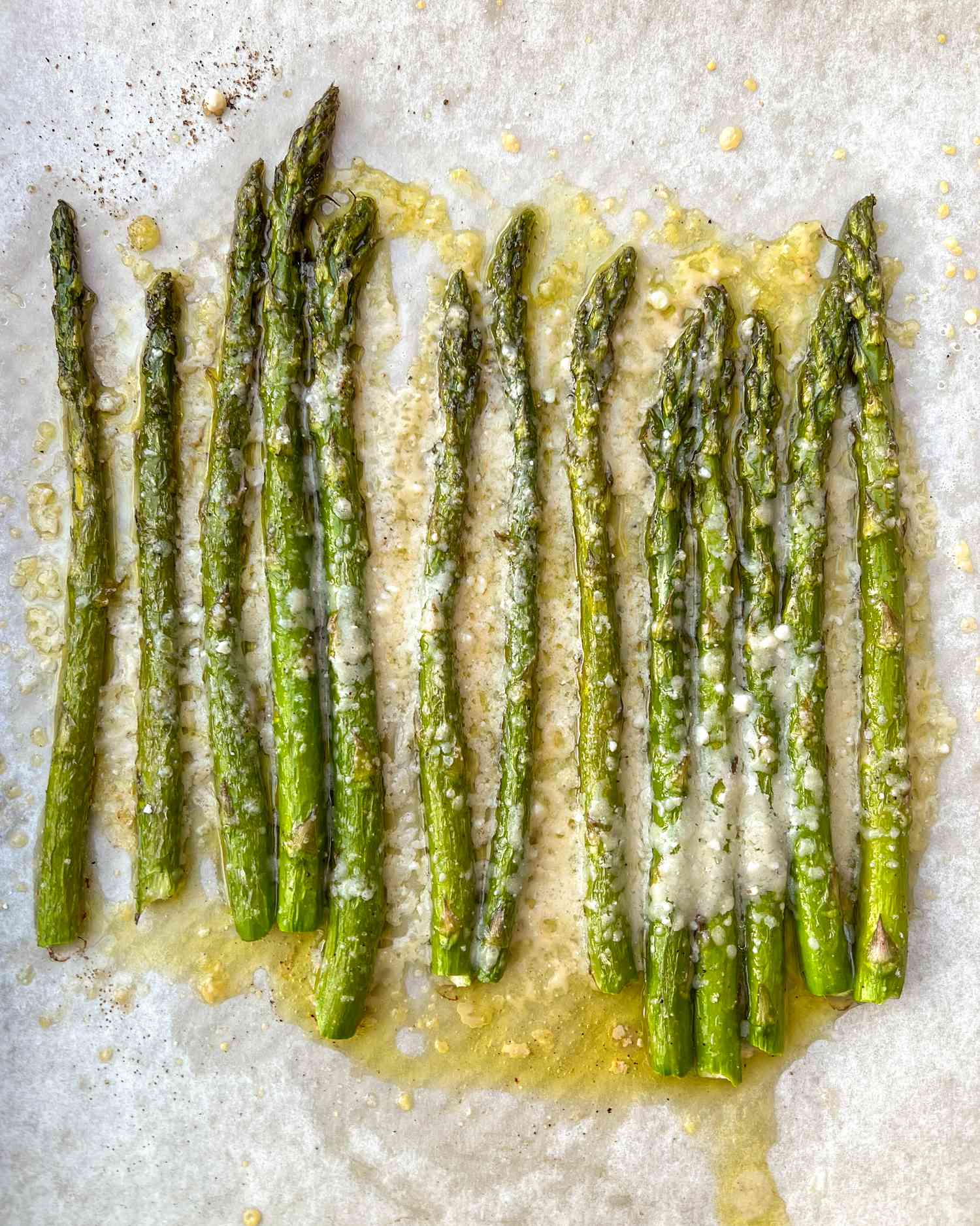 Roasted asparagus arranged on parchment paper with grated cheese