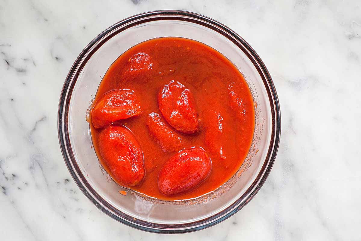 Tomatoes ready to be crushed in a glass bowl to make the best pasta sauce recipe.