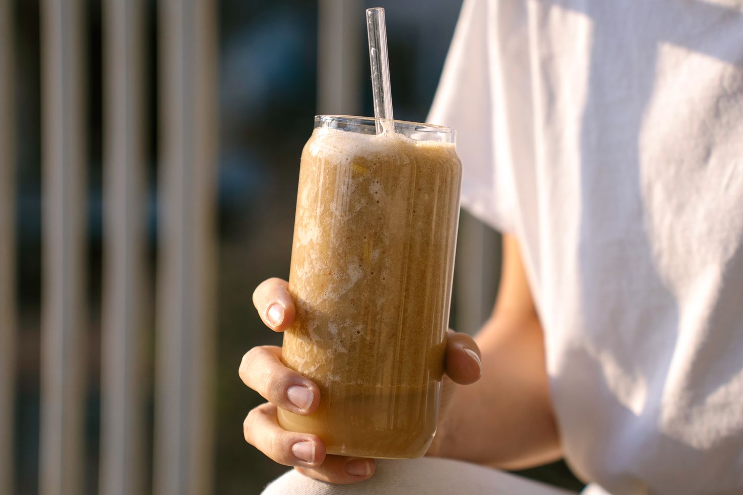 A hand holding a tall glass filled with a smoothie a straw in the drink