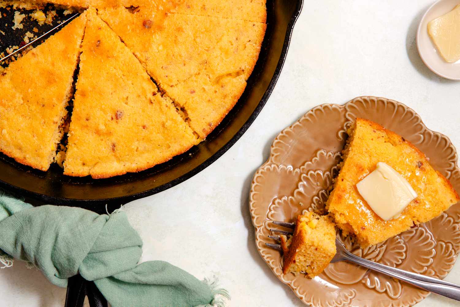 A wedge of cornbread on a plate next to a skillet with the rest of the cornbread inside