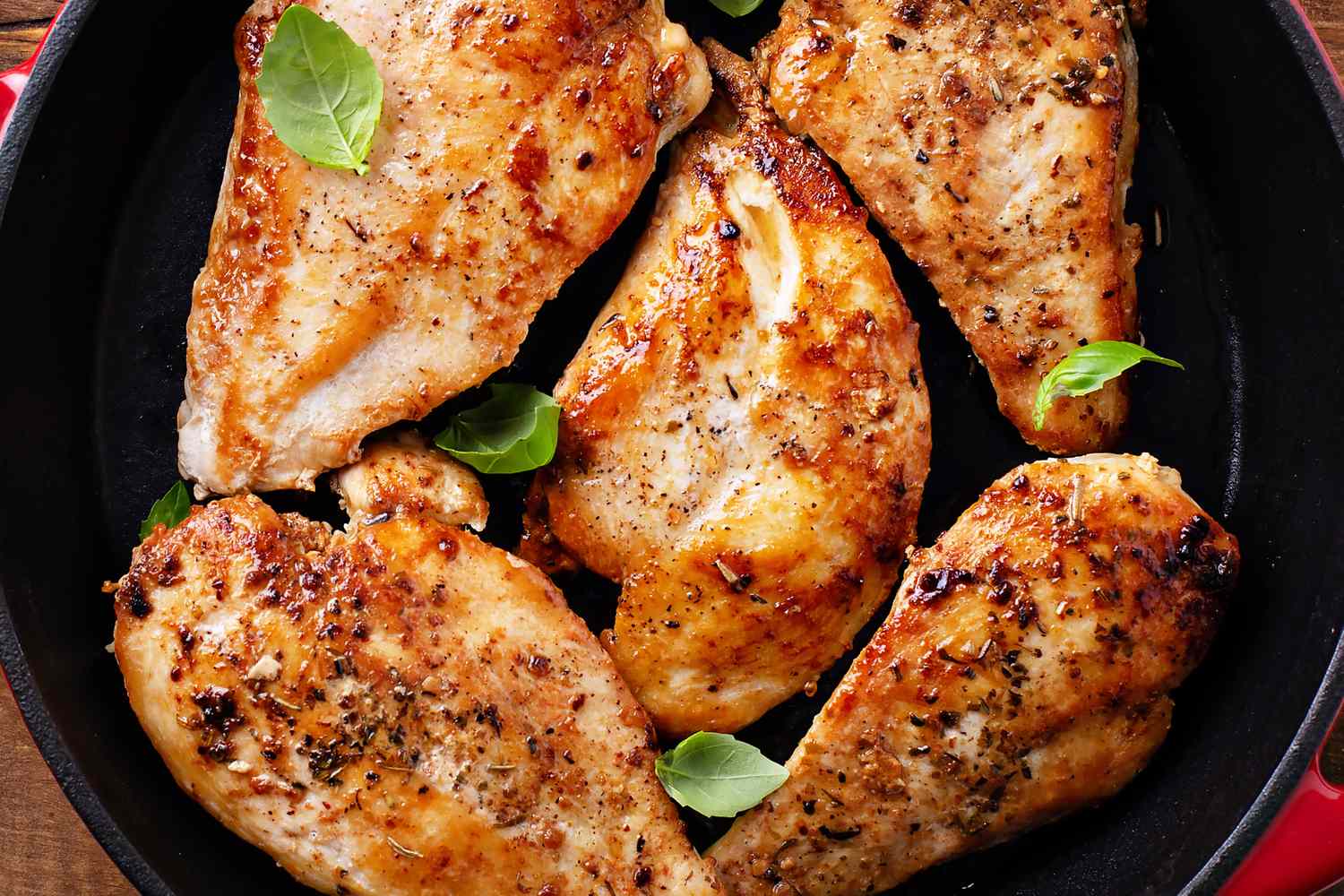 Cooked chicken breasts in a pan with a few fresh leaves as garnish