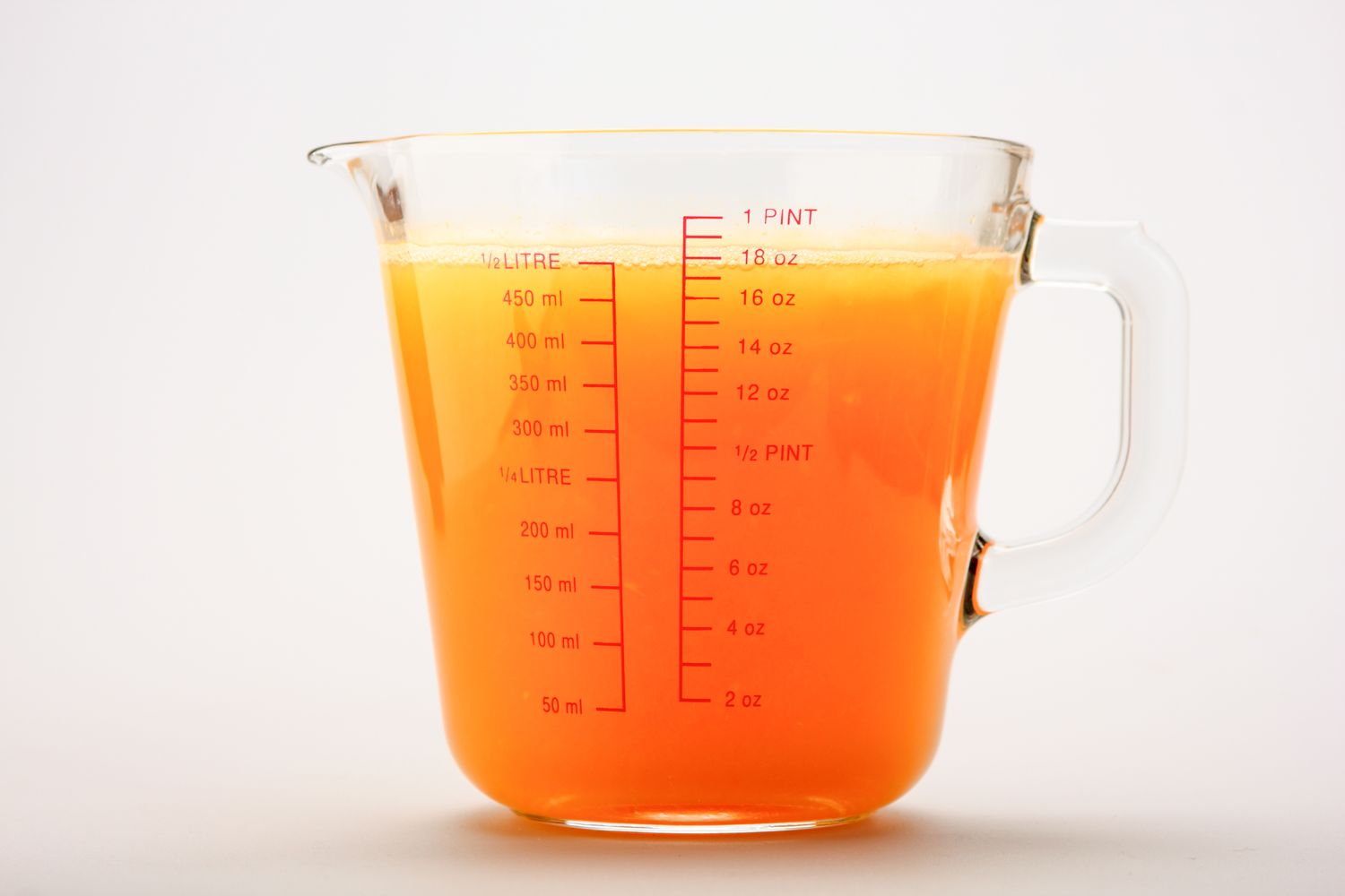 A clear measuring cup filled with orange liquid up to the onepint mark