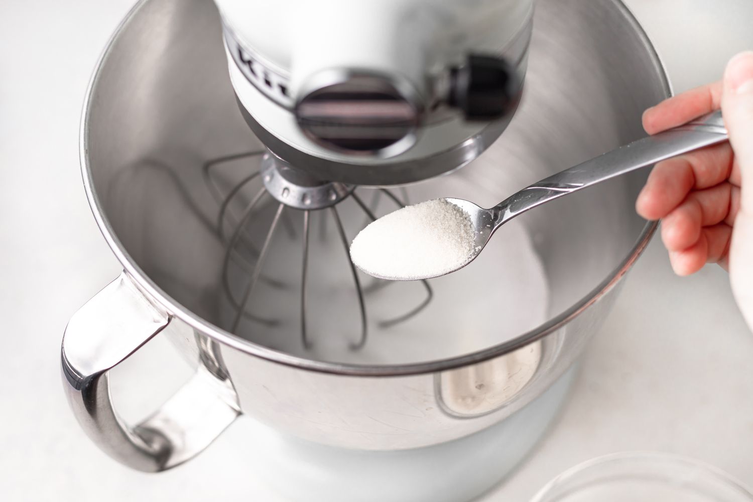 Adding sugar to a bowl to make the meringue for chocolate macarons.