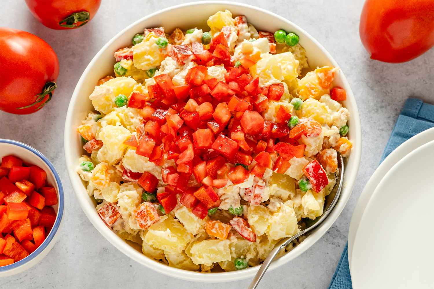 A dish of Ensalada Rusa topped with chopped tomatoes with vegetables like peas and carrots visible
