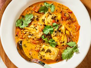 A bowl of moqueca Brazilian fish stew with fish pieces tomatoes herbs and broth garnished with cilantro