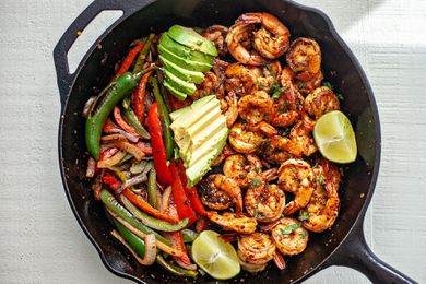 Shrimp Fajitas in a cast iron skillet topped with lime slices and avocado