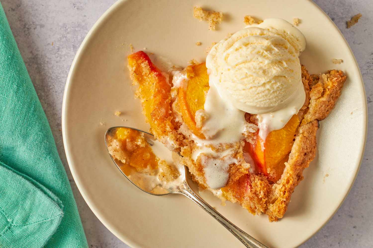 A plate with a slice of peach spoon cake topped with a scoop of ice cream