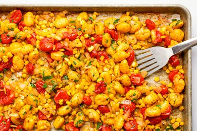 A close-up of cooked gnocchi with cherry tomatoes and corn on a sheet pan with a fork