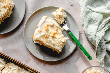 Overhead view of a gray plate of coconut cake with a fork next to a green cloth napkin