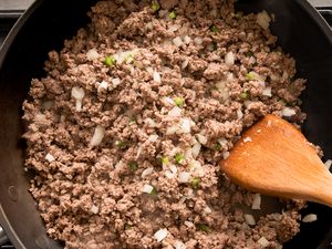 Cooking ground beef with diced onions in a skillet a wooden spoon stirring the mixture