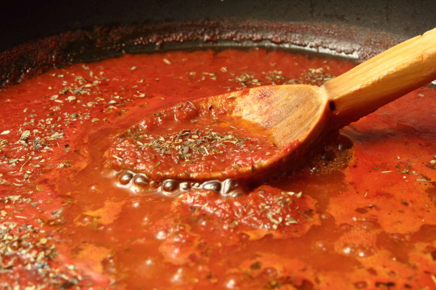 Wooden spoon stirring tomato sauce with herbs in a pan