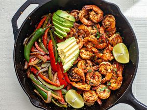 Shrimp Fajitas in a cast iron skillet topped with lime slices and avocado
