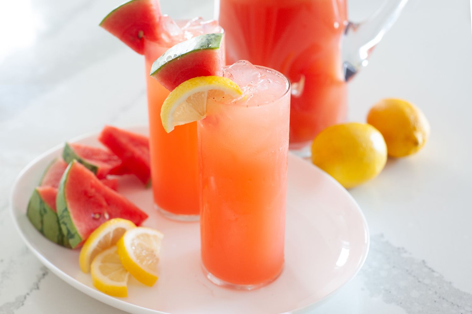 Whole lemon and watermelon lemonade in tall glasses and garnished with lemon and watermelon.