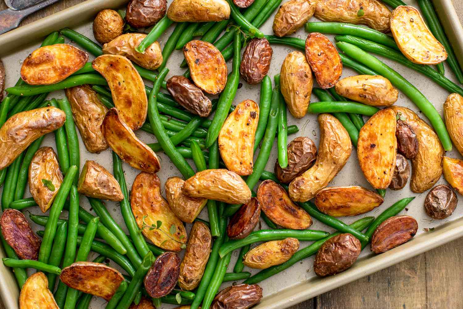 Roasted crispy fingerling potatoes with green beans on a sheet pan with herbs and spices, spring side dish