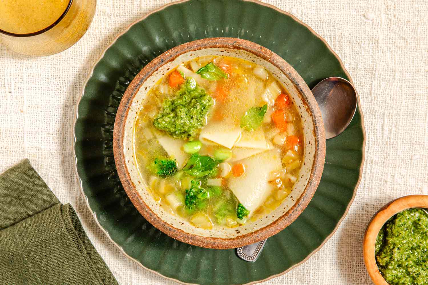 A bowl of Jamie Oliver's "Freezer Raid" Vegetable soup placed on a green serving plate with a spoon next to it