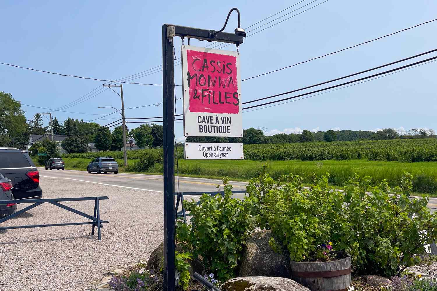 A roadside sign reading Cassis Monna Filles Cave Vin Boutique with a scenic rural backdrop
