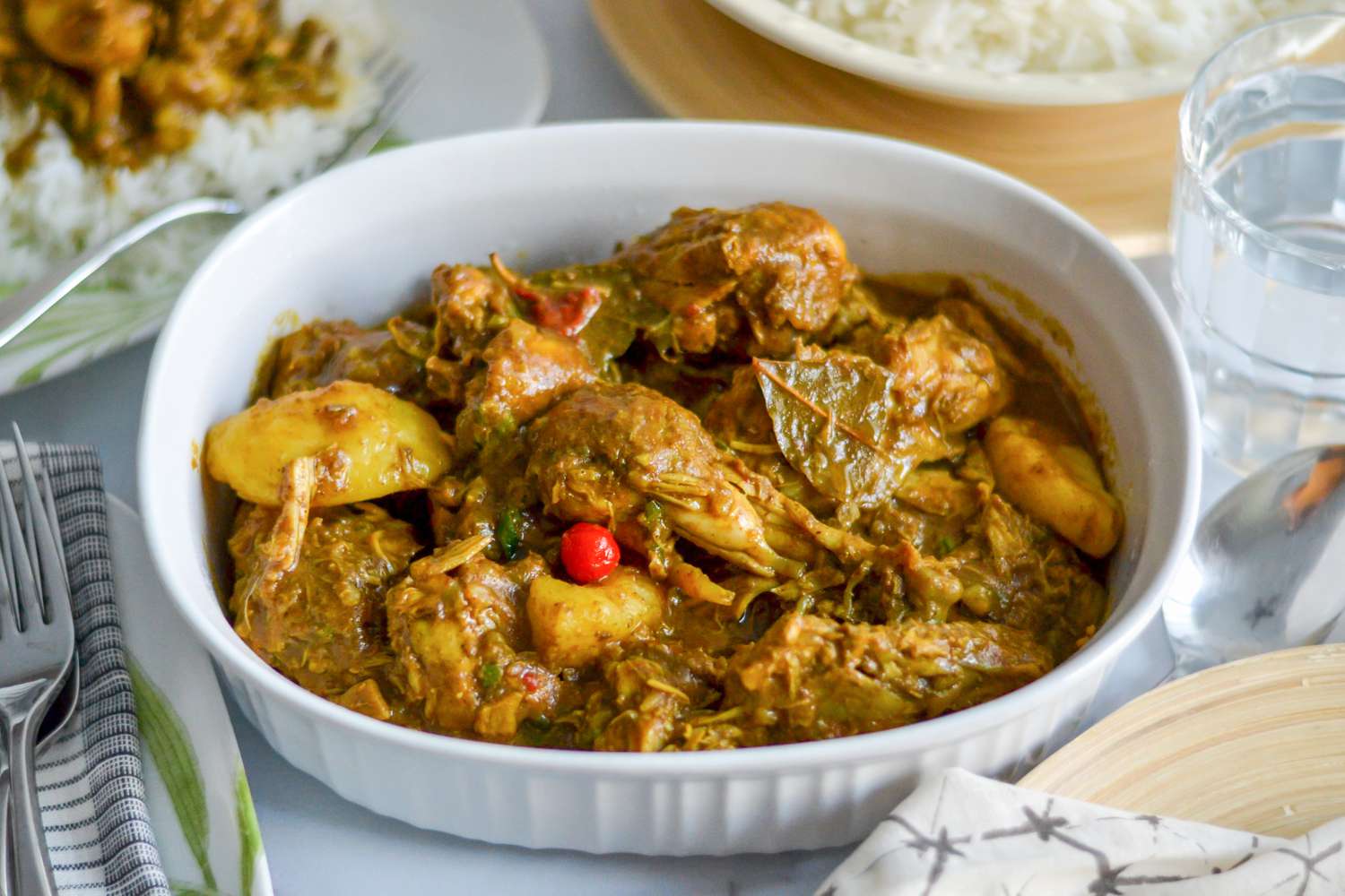 Guyanese Chicken Curry in a Baking Dish Surrounded by a Bowl of Rice and a Plate with a Serving