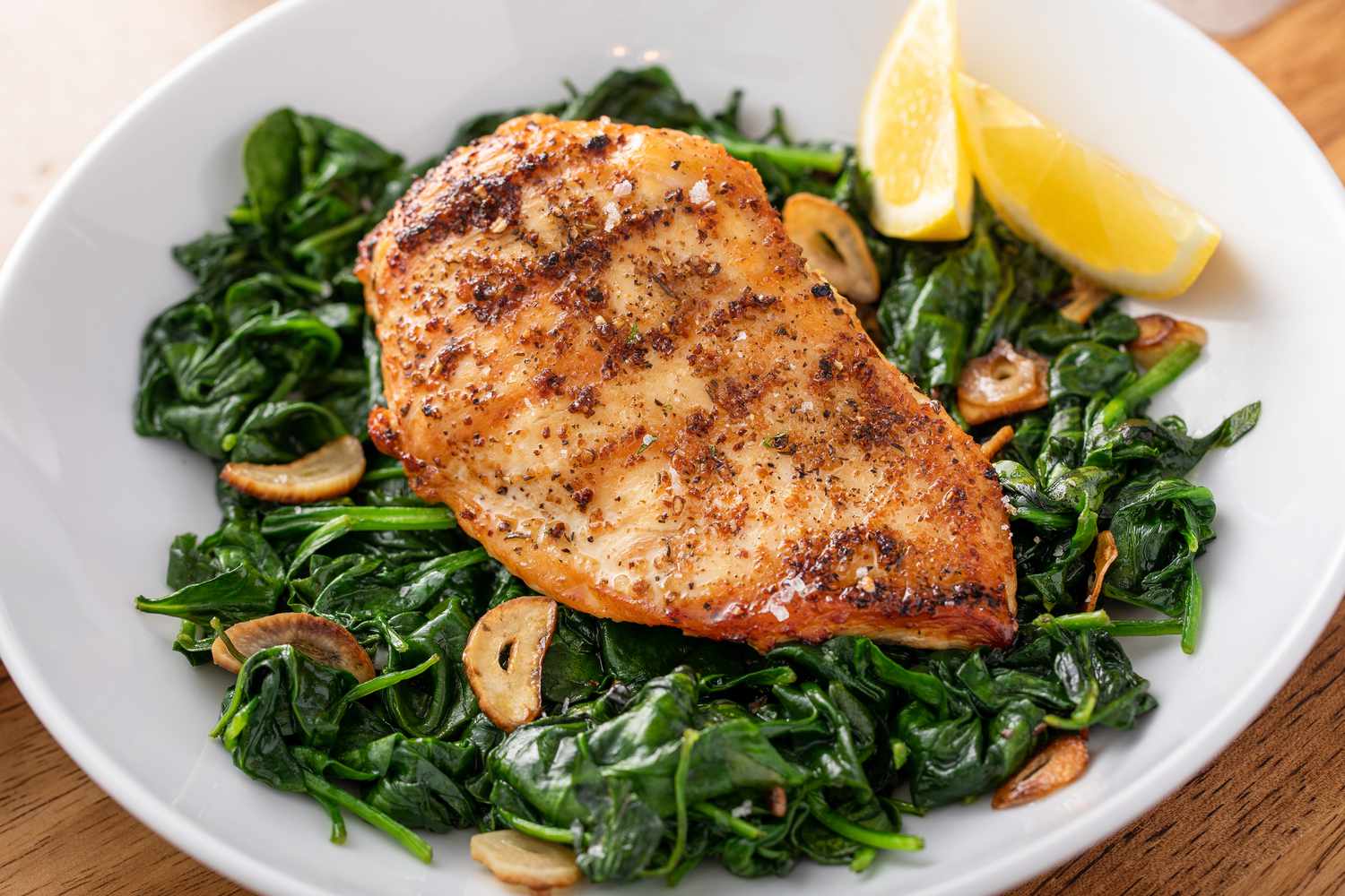 grilled chicken over a bed of sauteed spinach in a plate with lemon wedges