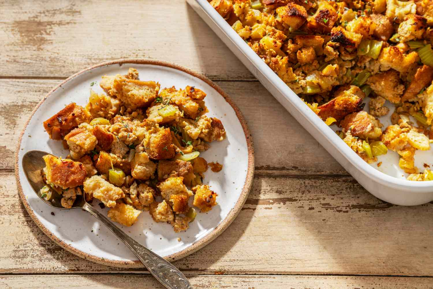 Thanksgiving stuffing served on a plate with a spoon with a casserole dish of stuffing in the background