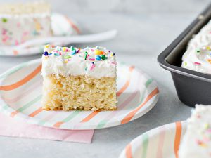 Easy Vanilla Cake Recipe - slice of vanilla cake with white frosting and sprinkles on striped paper plate.