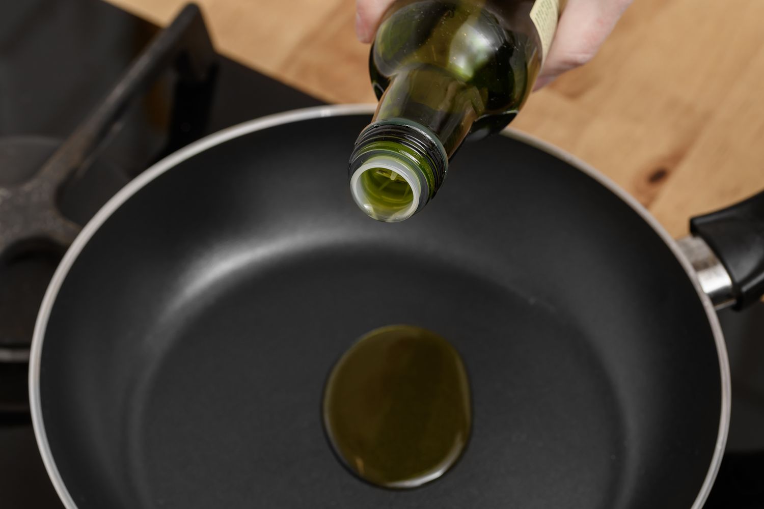 Pouring olive oil into a frying pan on a cooktop