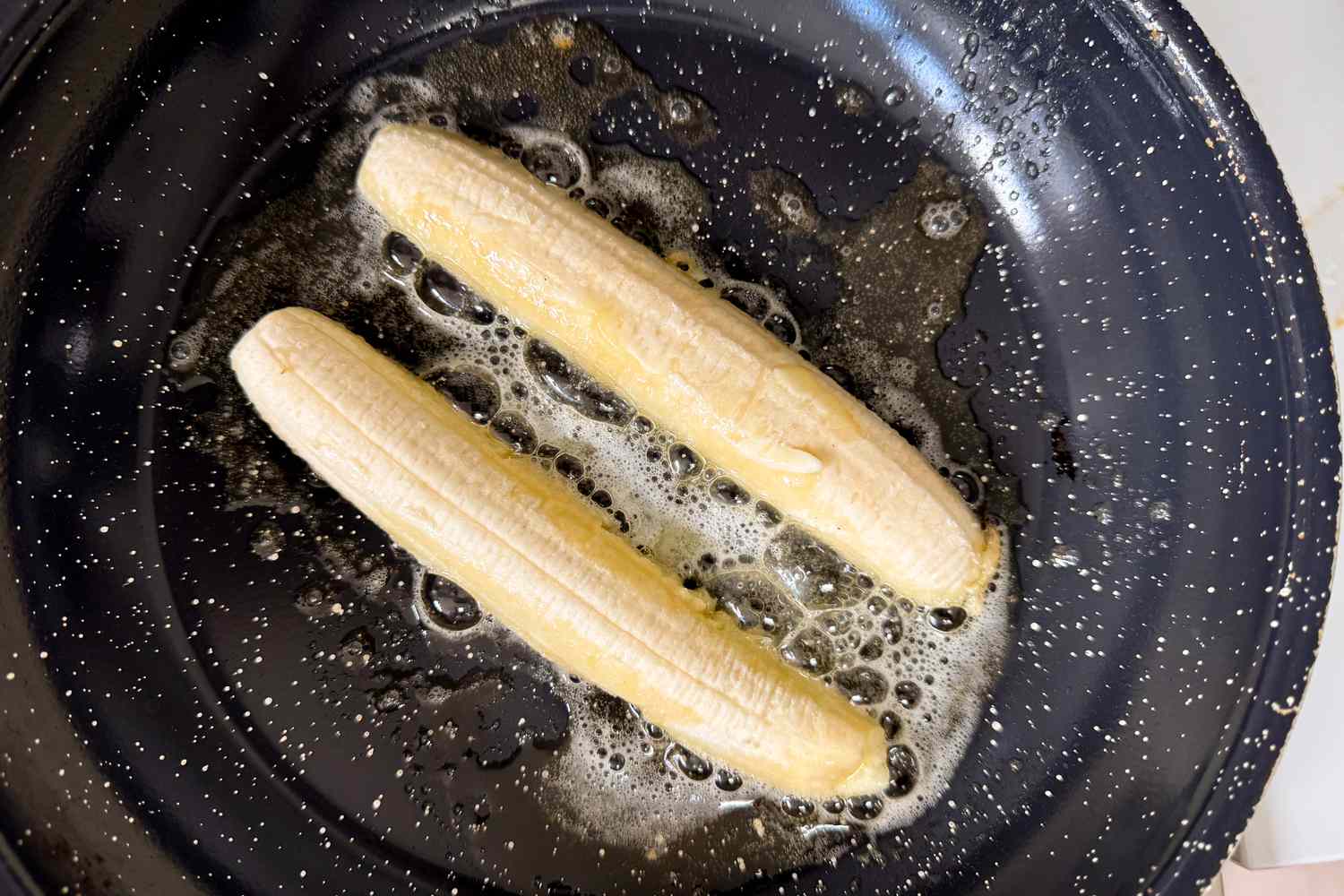 Two bananas cooking in a pan with melted butter