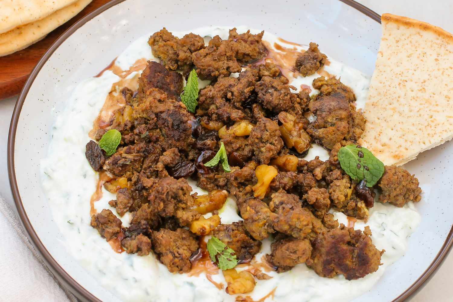 Dish featuring spiced ground meat over a creamy yogurt mixture garnished with mint leaves and served with flatbread