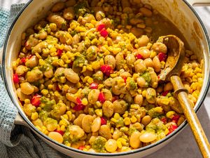 Pot of succotash with corn, lima beans, cherry tomatoes, seasoned sauce, wooden spoon on the side