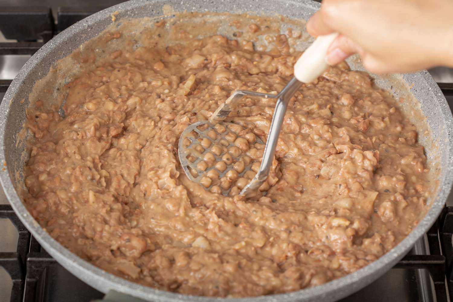 Mashing beans in a skillet with a potato masher