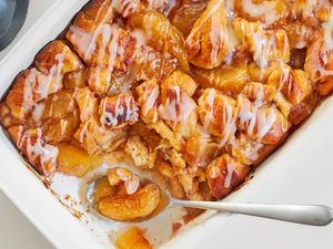 A baked apple cinnamon dish with icing in a white casserole pan a serving spoon scooping a portion from one end